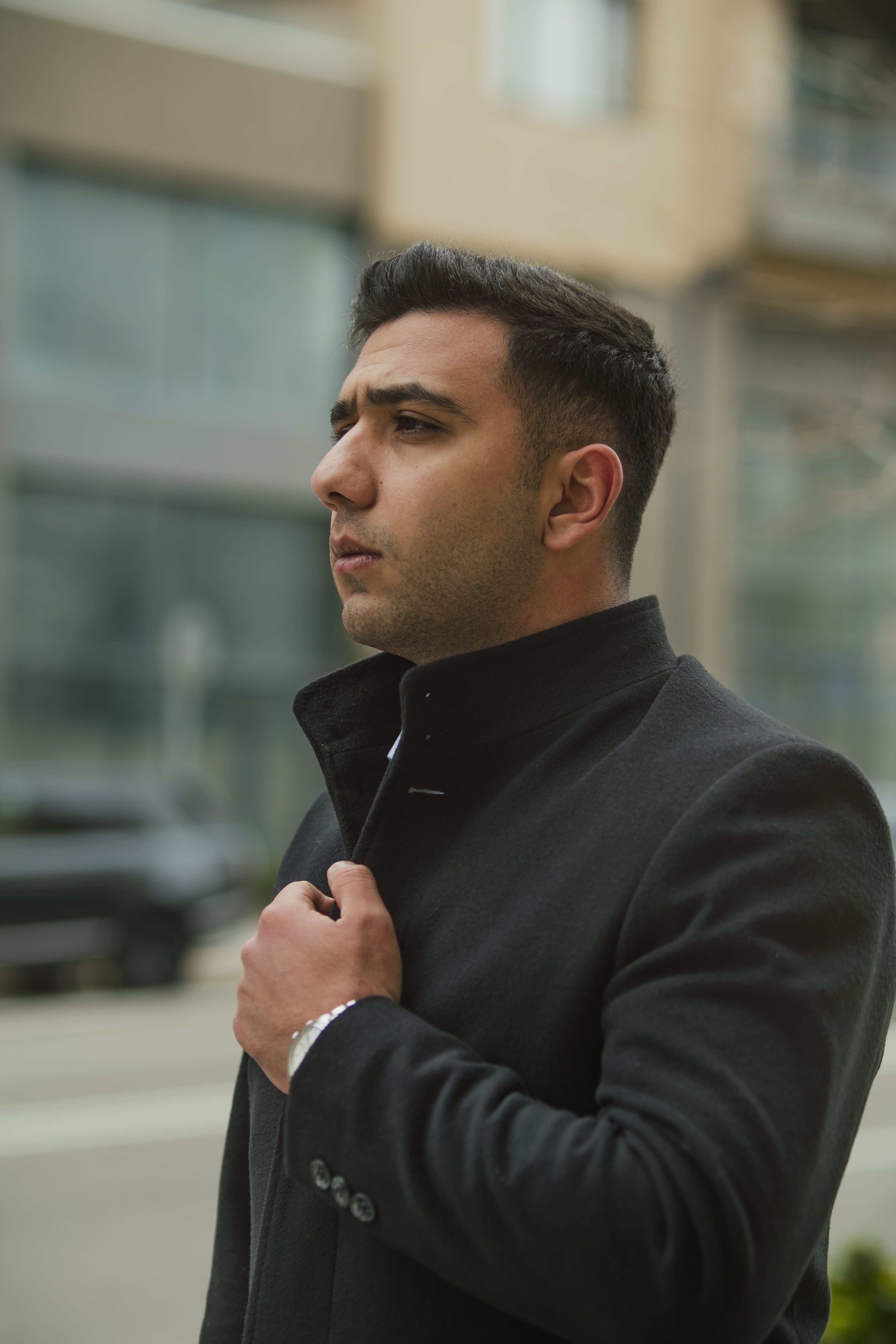Young man in a dark coat confidently posing on an urban street. Perfect for modern fashion or lifestyle themes.