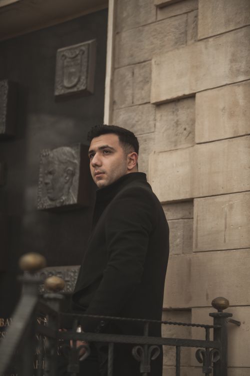 Free A fashionable man in a black coat walks by a stone wall displaying artistic reliefs, bringing an urban autumn vibe. Stock Photo