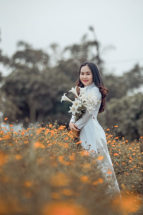 Free A beautiful woman in traditional wear holding a bouquet in a flower field. Stock Photo