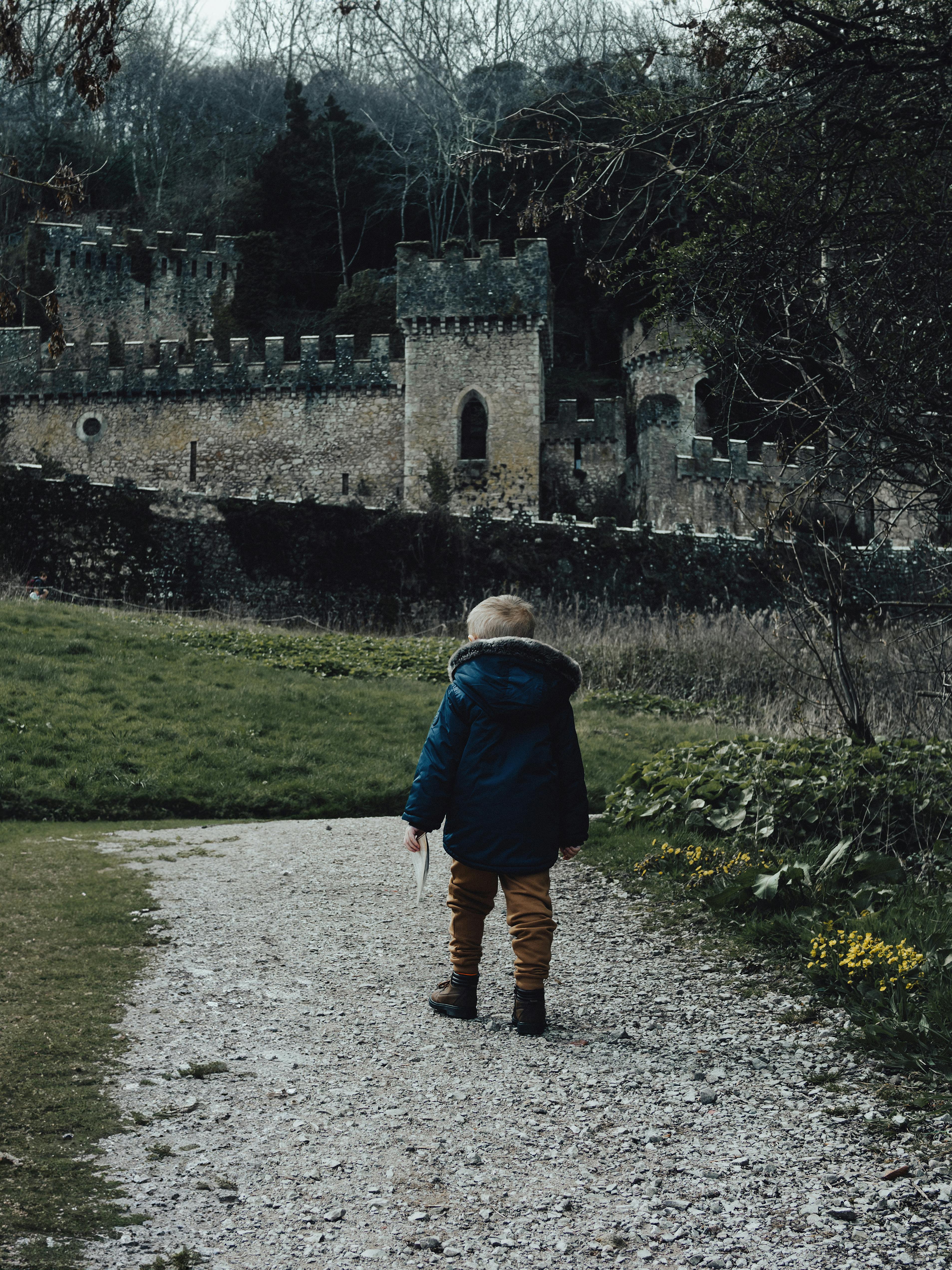 Young child walking towards Gwrych Castle ruins in Abergele, UK, surrounded by lush countryside.