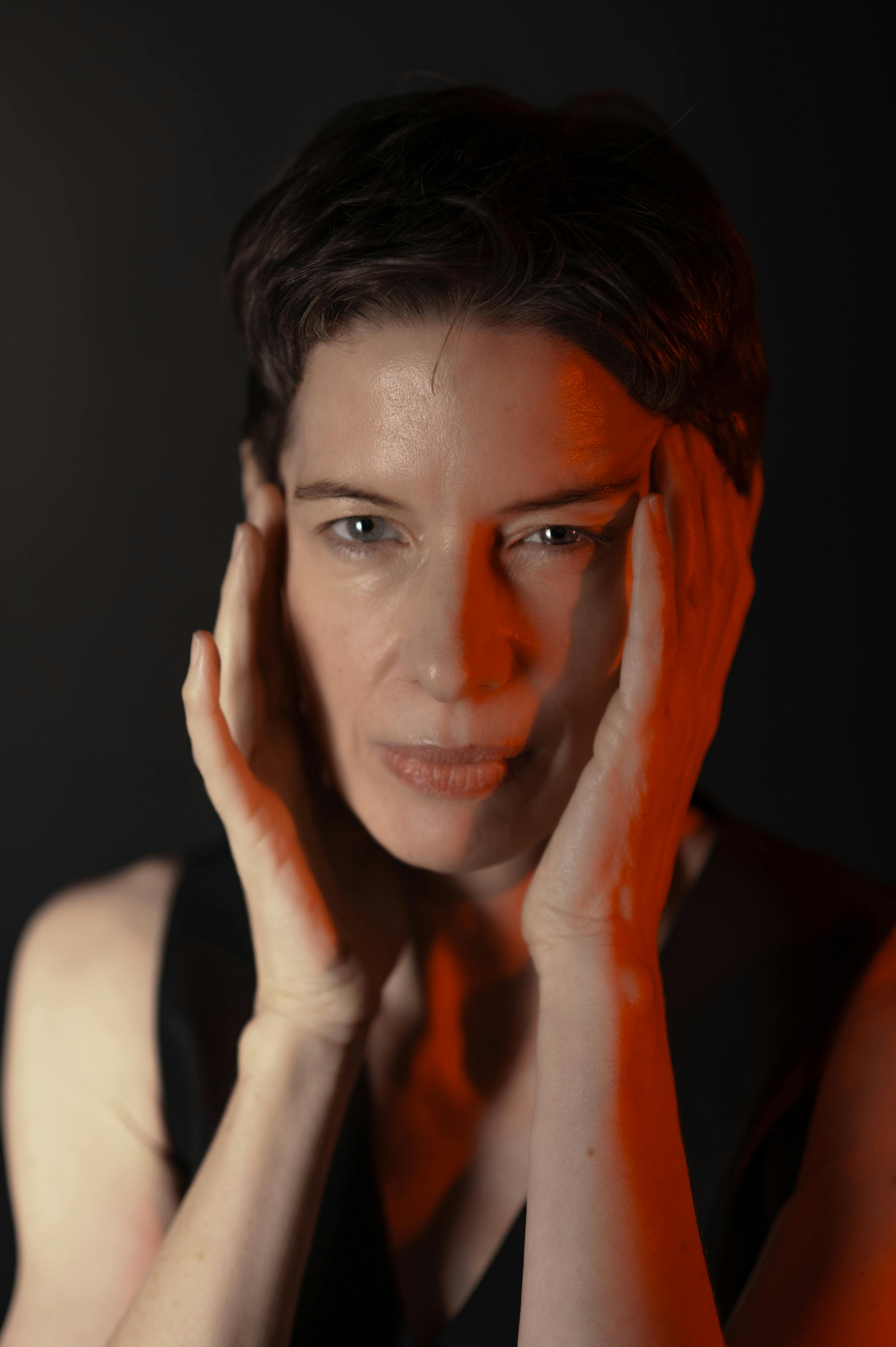 Artistic portrait of a woman with hands on cheeks and dramatic red lighting, emphasizing emotion.