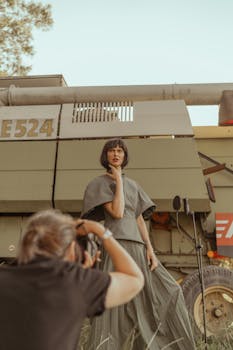 Fashion photoshoot featuring a model posing near a combine harvester outdoors.