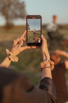 A woman captures a man in rural Oświęcim with a smartphone in a serene setting.