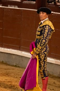A matador in ornate traditional costume stands in a Madrid bullring holding a cape.