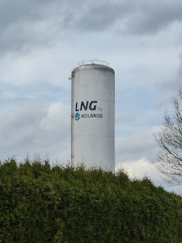 Vertical LNG storage silo by Rolande surrounded by greenery and cloudy sky.