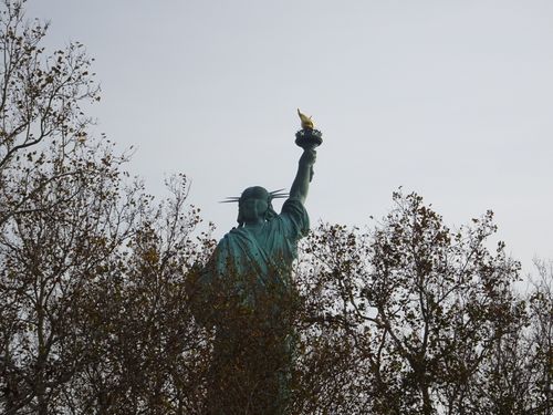 Free Back view of the Statue of Liberty with autumn trees, highlighting the iconic torch. Stock Photo