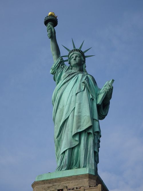 Free Iconic Statue of Liberty against a blue sky, symbolizing freedom and democracy. Stock Photo