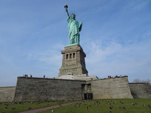 Free The Statue of Liberty stands tall against a blue sky in New York City, surrounded by birds. Stock Photo