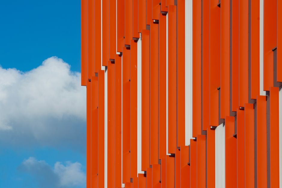 Striking modern architecture with vibrant orange panels against a clear blue sky in Rotterdam.
