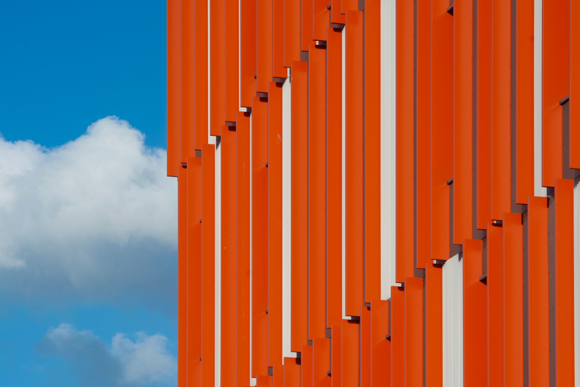 Striking modern architecture with vibrant orange panels against a clear blue sky in Rotterdam.