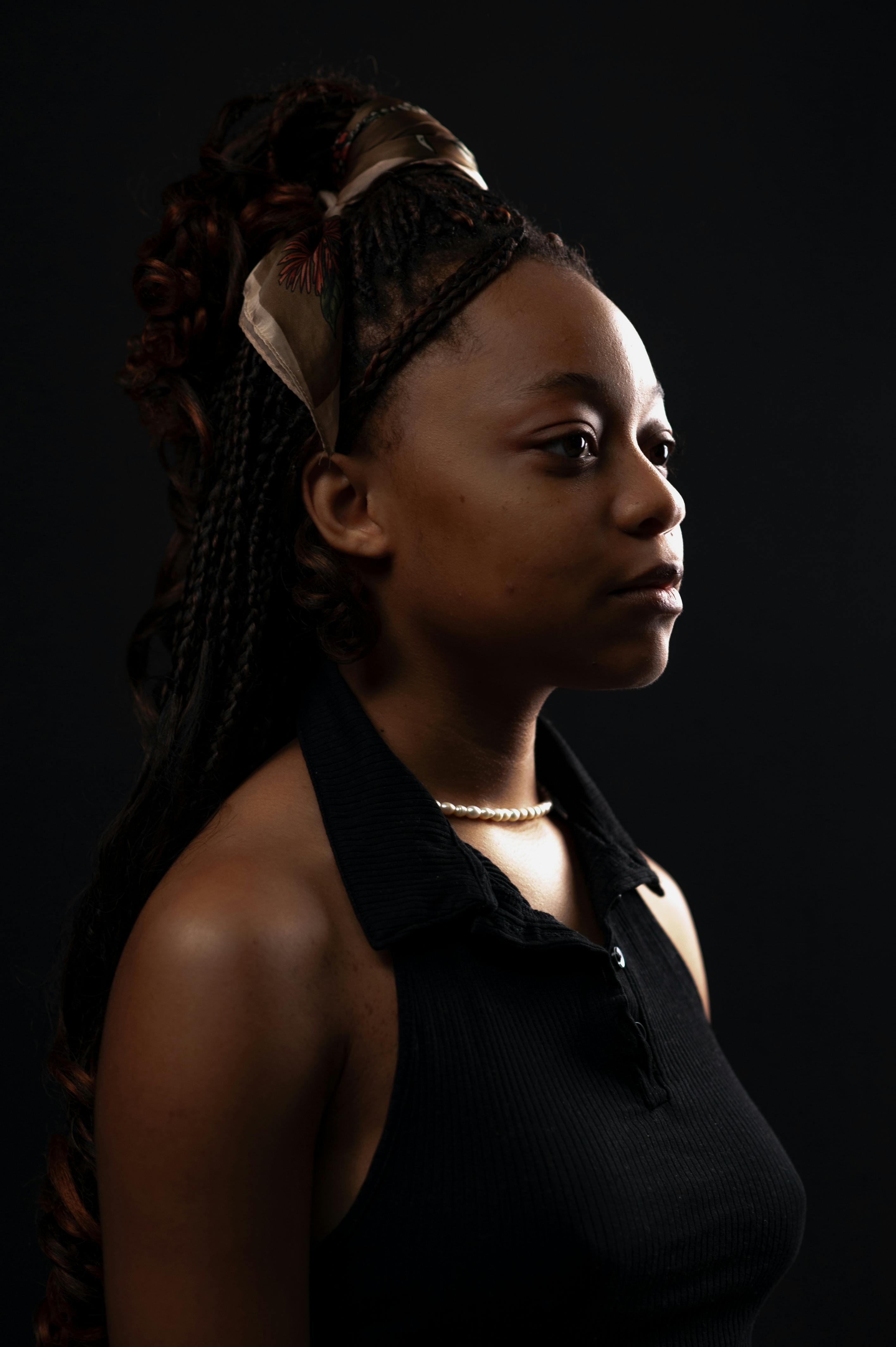 Free Elegant studio portrait of a woman in a black tank top with a braided hairstyle on a dark background. Stock Photo