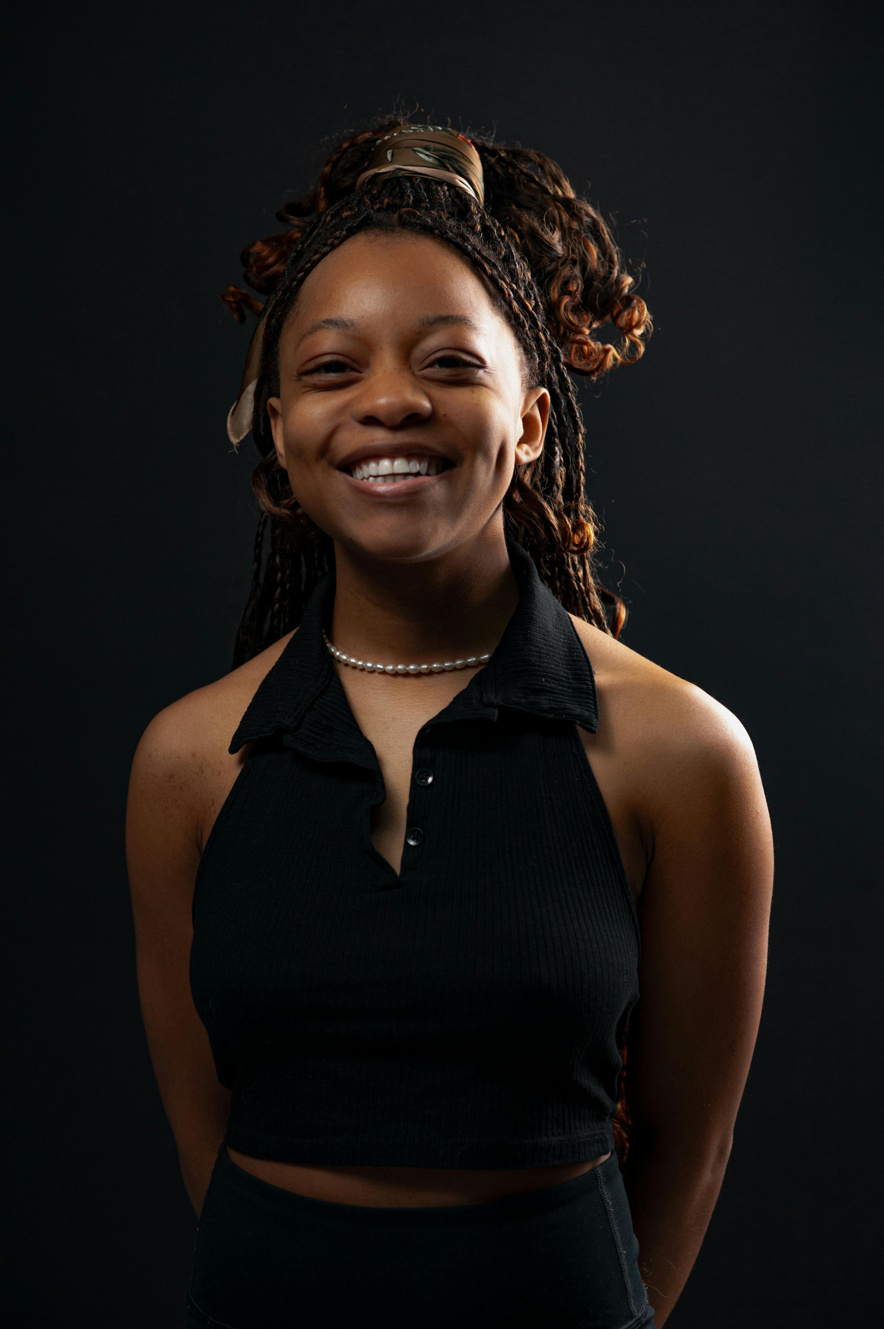 Free Portrait of a smiling Black woman in a studio shoot with a dark background wearing a black tank top. Stock Photo