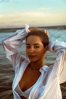 Portrait of a stylish woman in a white shirt embracing the sea breeze at sunset.
