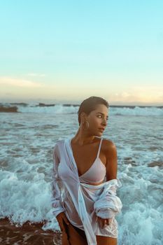 Stylish woman in wet white shirt posing by the sea during summer.