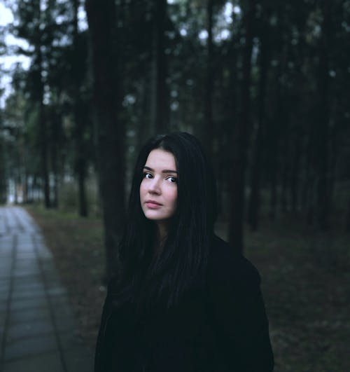 A woman with long black hair standing in the woods