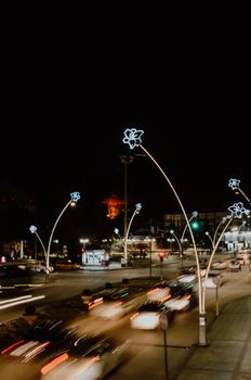 A bustling city street at night with blurred car lights and illuminated decorations, capturing urban nightlife.