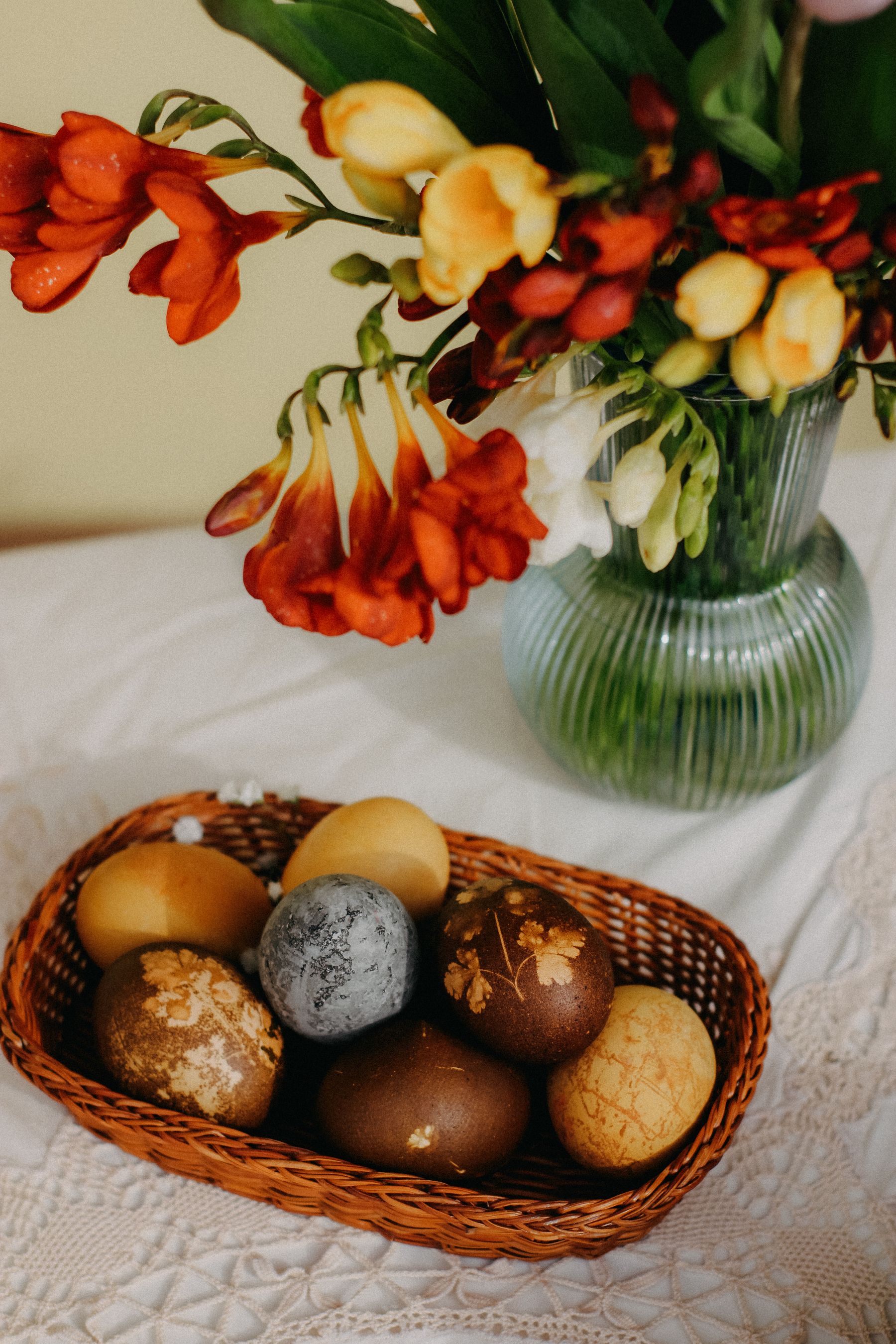 Colorful Easter eggs grouped in a wicker basket beside spring flowers