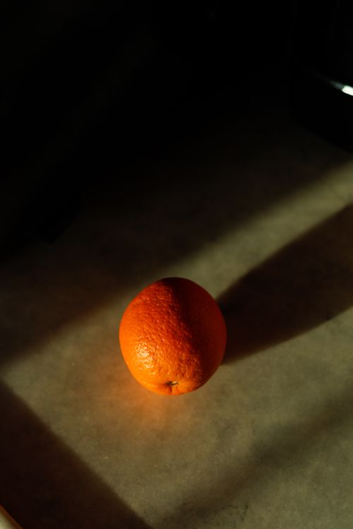 Free A single orange in dramatic sunlight casting shadows on a surface. Stock Photo