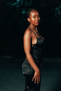 A stylish young woman in a black dress posing elegantly outdoors at dusk.