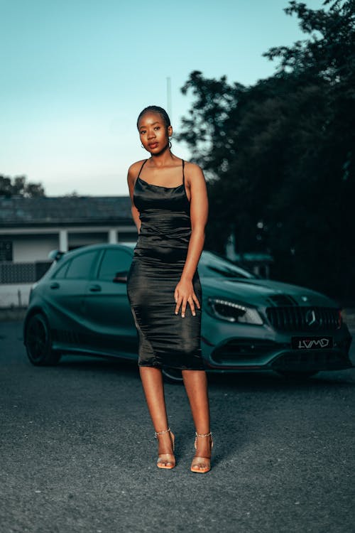 A woman in a black dress standing next to a car
