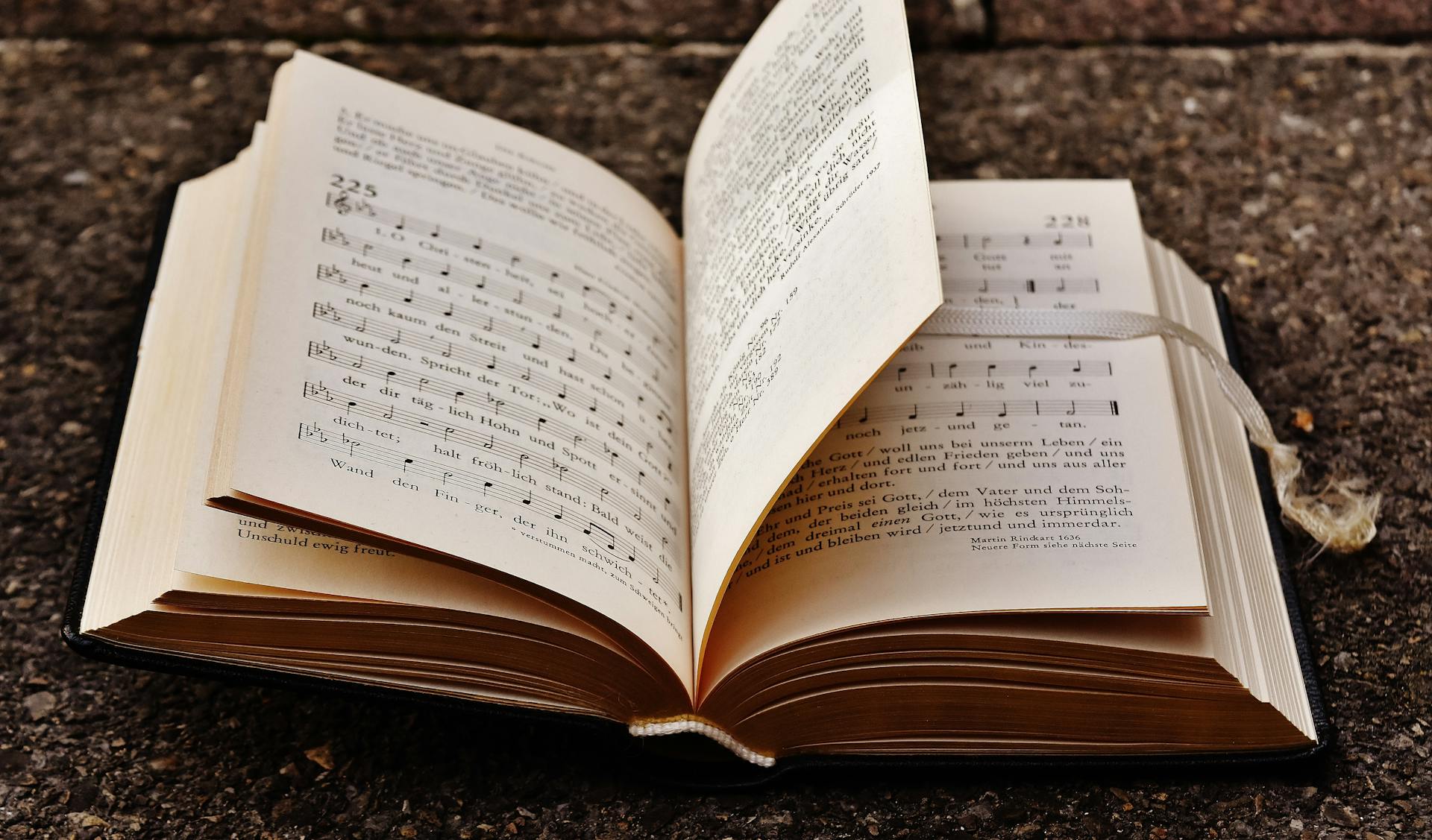 An open hymnal resting on a stone surface displaying musical notes and text.