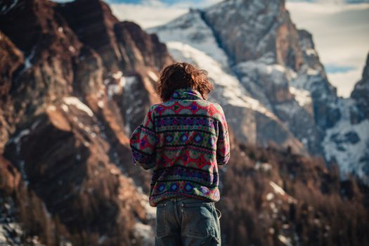 Back view of a woman in colorful sweater admiring the snowy mountains of Fiera di Primiero.