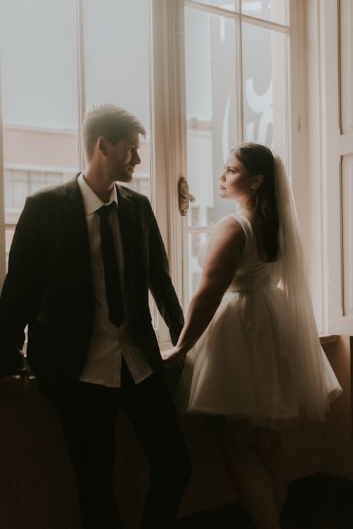 A bride and groom standing in front of a window