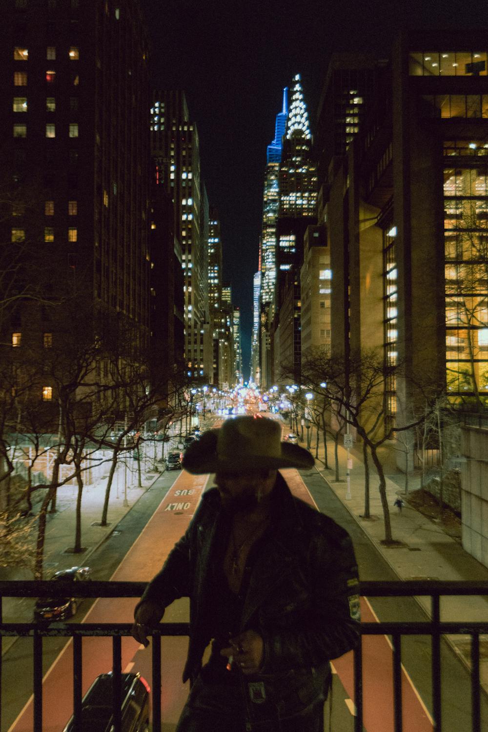 Man Standing on a Balcony with New York City by Night in the Background ...
