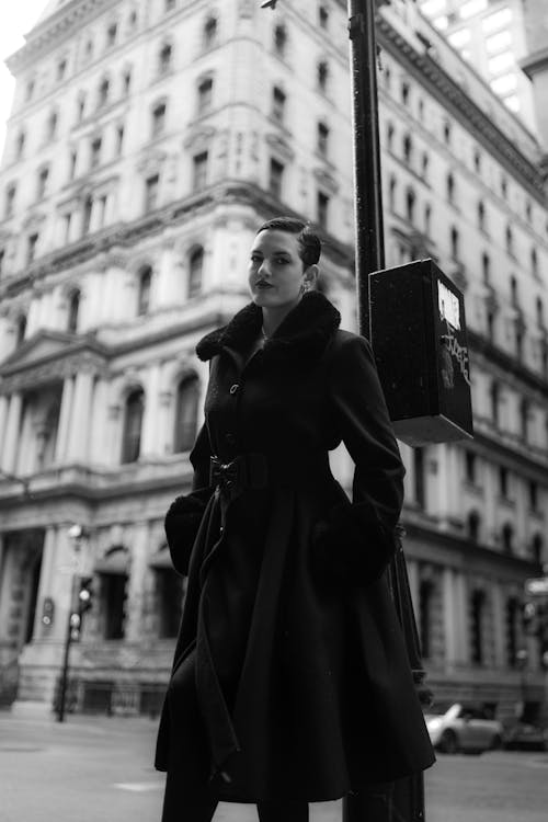 A woman in a black coat and hat standing on a street corner