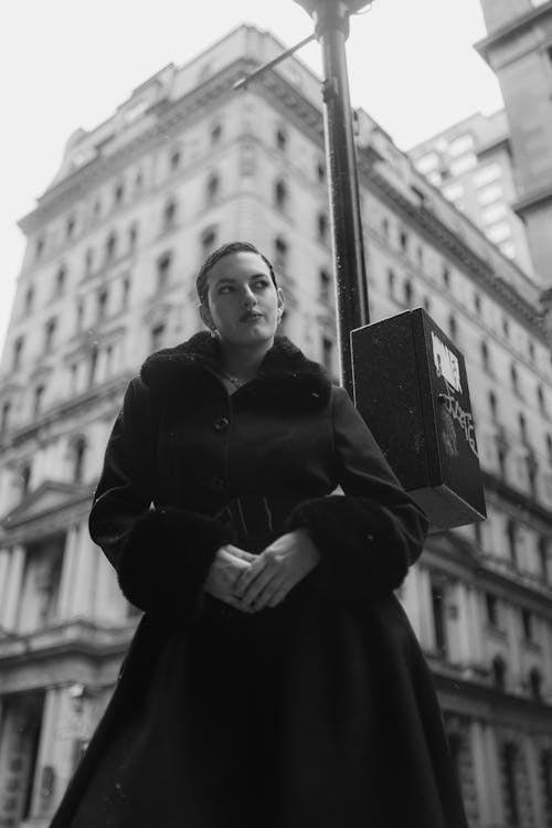 A woman in a black coat and hat standing on a street corner