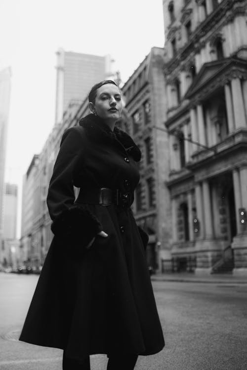 A woman in a black coat and hat standing on a city street