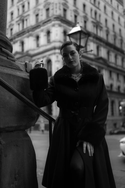 Black and white photo of woman in coat leaning on stairs