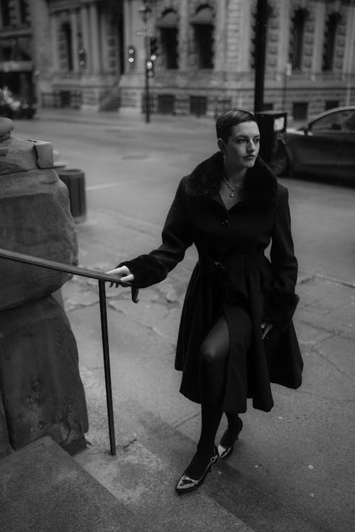 A woman in a black coat and stockings is standing on the steps