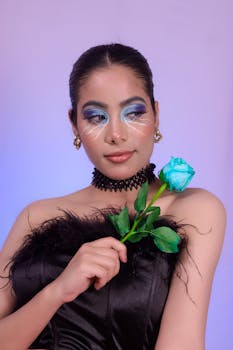A stylish portrait of a woman with artistic makeup holding a vibrant blue rose, exuding elegance.