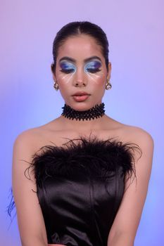 Elegant portrait of a woman in black dress with bold makeup against purple backdrop.