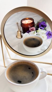 A cozy scene featuring a coffee cup, candle, and flowers reflected in a mirror, perfect for relaxation themes.