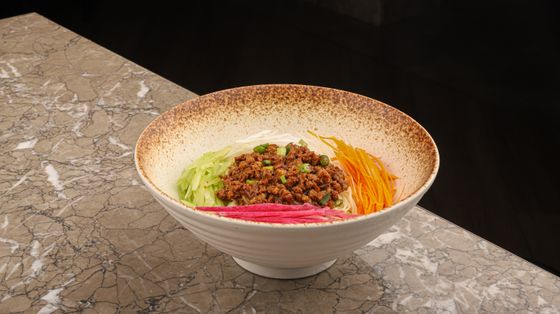 Noodles topped with minced pork bean sauce, cucumber, cabbage, carrot and radish strips in a bowl