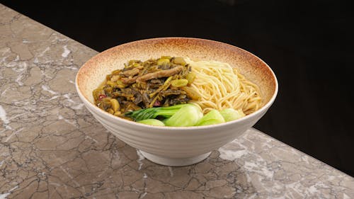 A bowl of noodles and vegetables on a marble counter