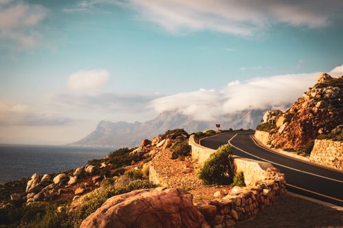 Free Discover the tranquil beauty of a winding coastal road set against a dramatic mountain backdrop, ideal for travel inspiration. Stock Photo