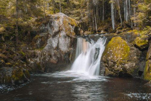 Free Peaceful waterfall flowing through a lush forest during autumn. Perfect for nature-themed projects. Stock Photo