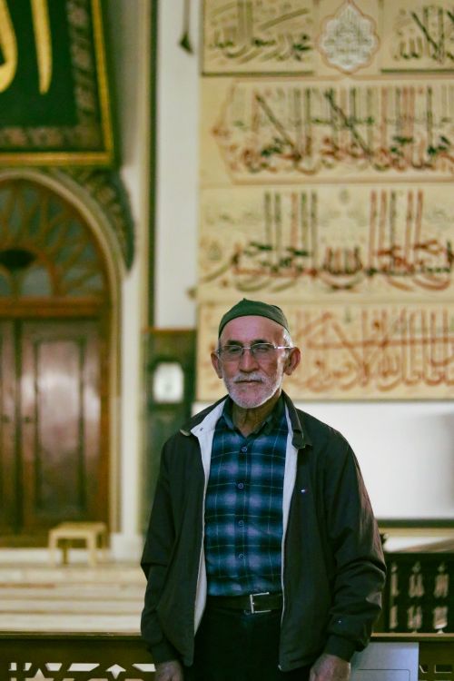 Free Senior man stands in a historical mosque with Arabic calligraphy on the walls, showcasing Islamic culture. Stock Photo