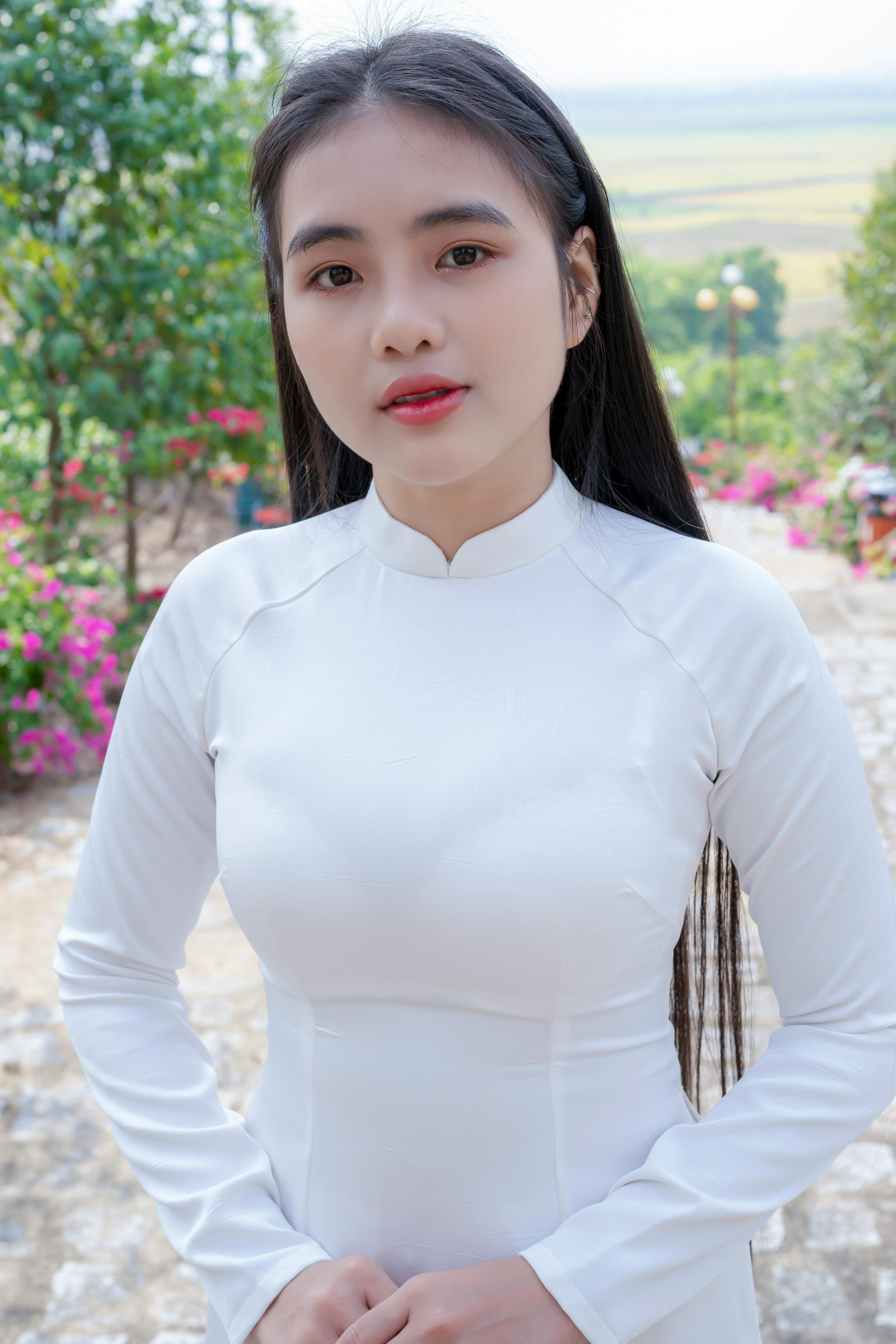 Portrait of a woman in a traditional white dress standing outdoors with a serene background.
