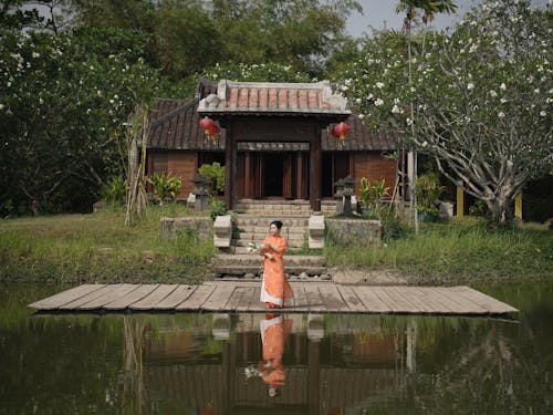 A woman in orange dress standing on the dock near a house