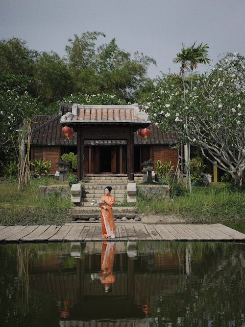 A woman in orange robes stands in front of a house