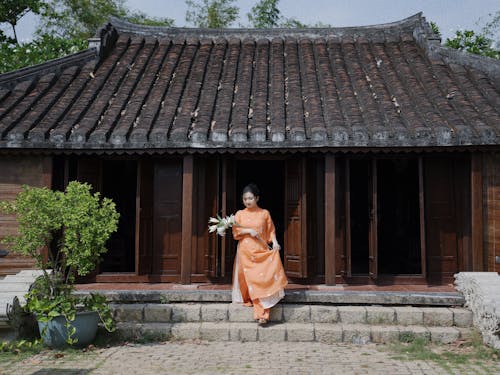 A woman in an orange dress stands outside a wooden building