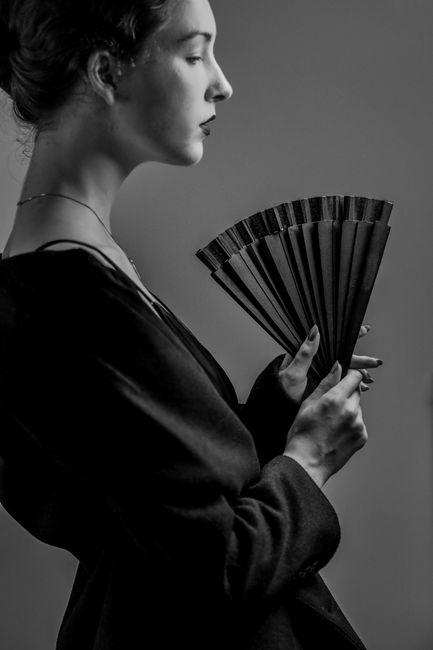 Stylish black and white portrait of a woman holding a fan in Paris studio.