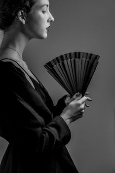 Black and white portrait of an elegant woman holding a fan, evoking classic fashion in a Paris studio.