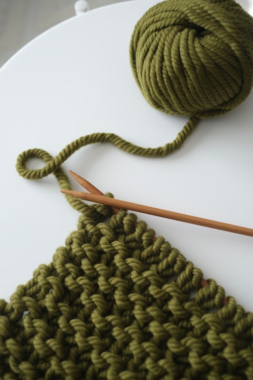 A knitting needle and yarn are next to a green crochet