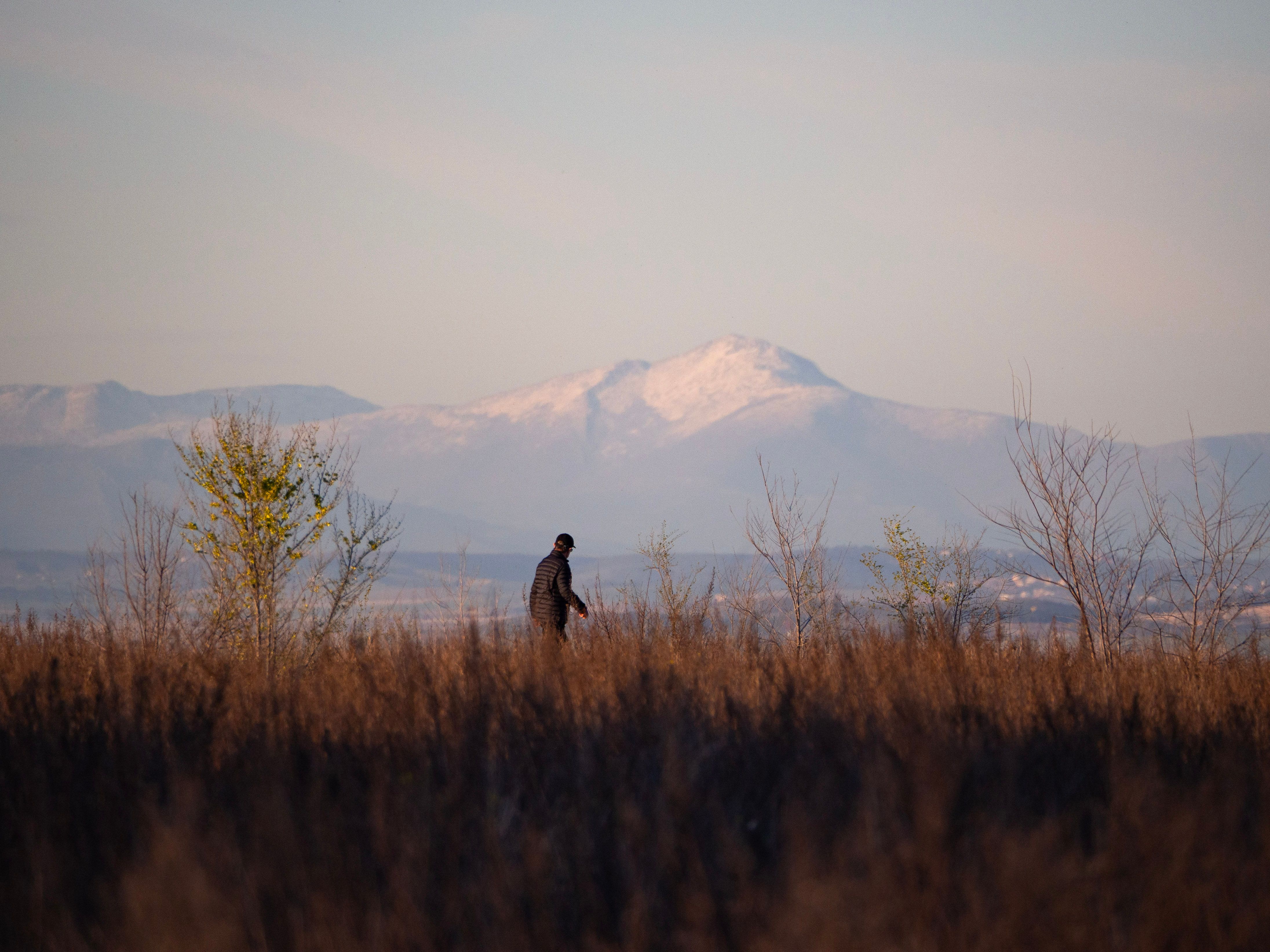 A lone man walks through a grassy field with mountains in the background under autumn skies near Coslada, Spain.