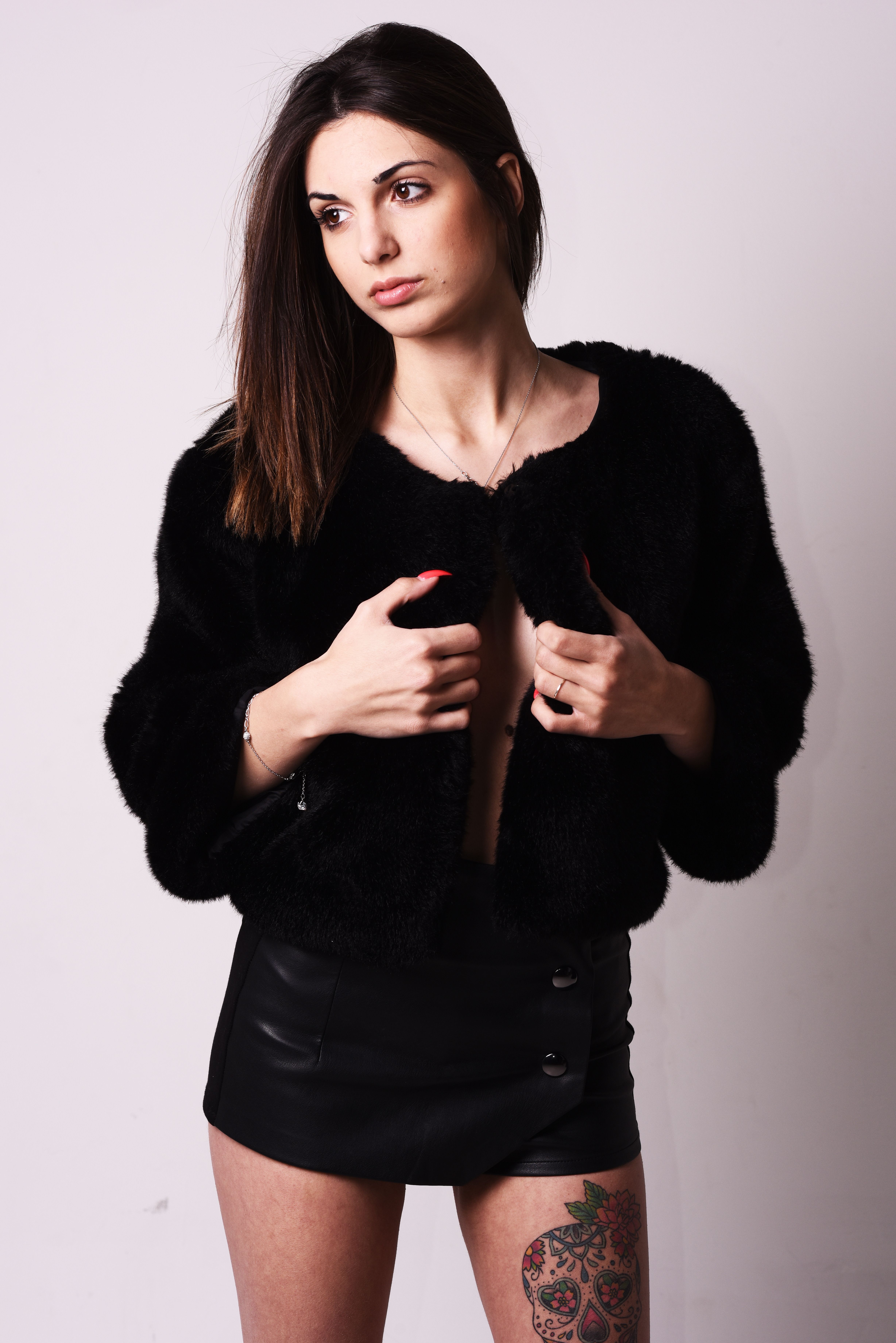 Portrait of a stylish woman posing in a fur jacket and mini skirt in a studio setting.